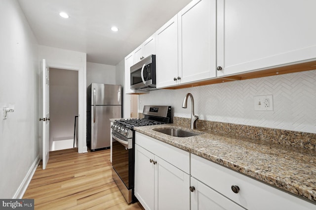 kitchen with appliances with stainless steel finishes, light stone counters, sink, light hardwood / wood-style flooring, and white cabinets