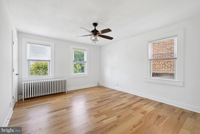 unfurnished room with a textured ceiling, light wood-type flooring, radiator, and ceiling fan