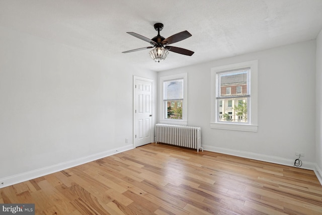 empty room with a textured ceiling, light hardwood / wood-style flooring, radiator, and ceiling fan