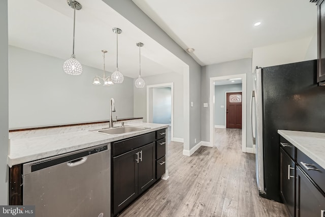 kitchen with light stone counters, stainless steel appliances, pendant lighting, sink, and light hardwood / wood-style flooring