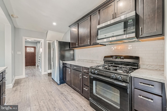 kitchen featuring light stone counters, appliances with stainless steel finishes, dark brown cabinets, light hardwood / wood-style flooring, and decorative backsplash