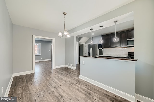 kitchen with pendant lighting, backsplash, appliances with stainless steel finishes, and hardwood / wood-style flooring