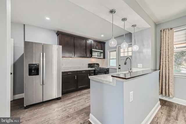 kitchen with backsplash, appliances with stainless steel finishes, dark brown cabinetry, pendant lighting, and light hardwood / wood-style flooring