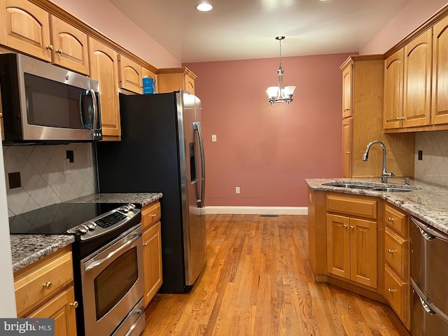 kitchen featuring stainless steel appliances, light hardwood / wood-style floors, sink, light stone countertops, and pendant lighting