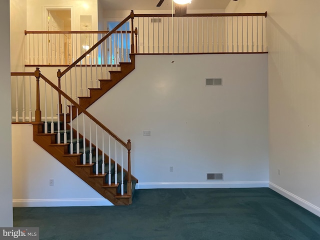 stairway with a towering ceiling, ceiling fan, and carpet