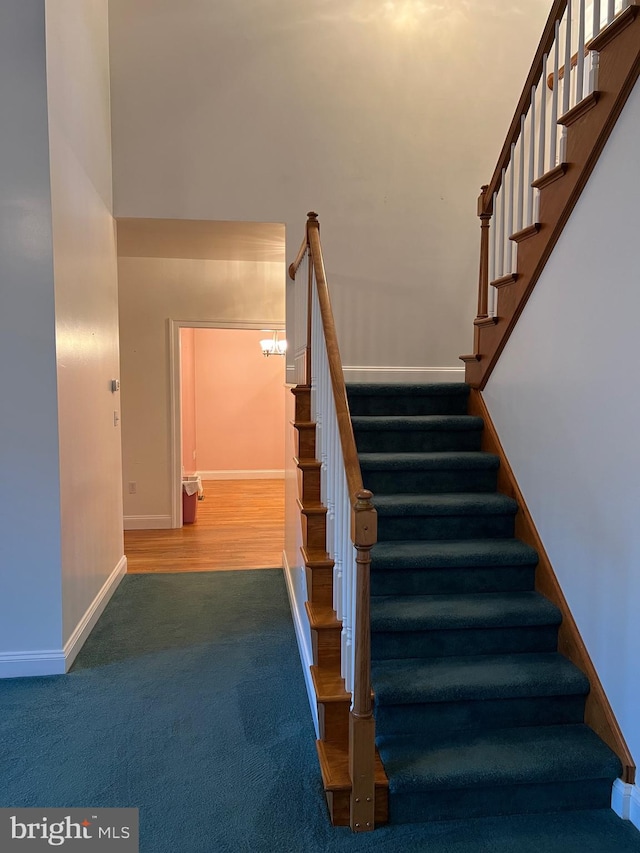 staircase with hardwood / wood-style floors, a high ceiling, and a chandelier