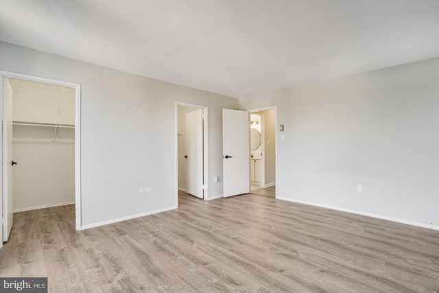 unfurnished bedroom featuring light wood-type flooring, a walk in closet, and a closet