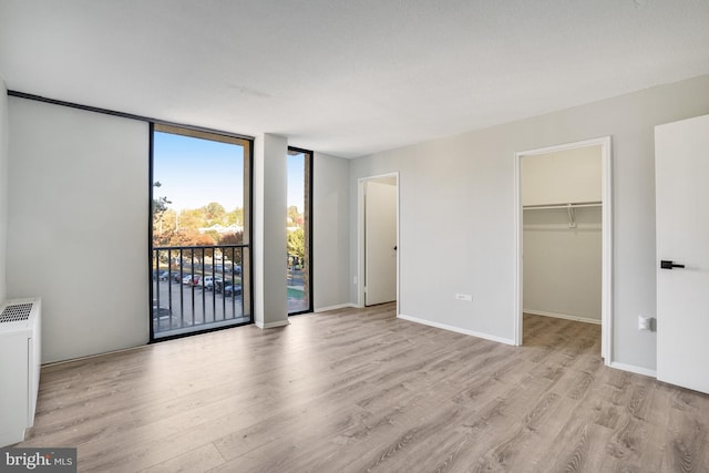 unfurnished bedroom with light hardwood / wood-style floors, access to exterior, floor to ceiling windows, a closet, and a walk in closet