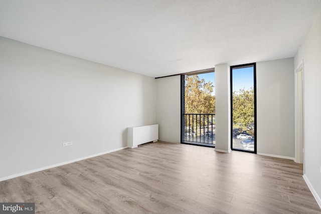 unfurnished room featuring radiator, light wood-type flooring, and expansive windows