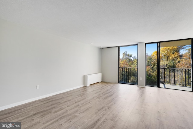 empty room with expansive windows, light hardwood / wood-style flooring, a textured ceiling, and radiator