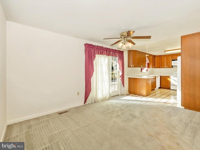 kitchen with stove, light colored carpet, ceiling fan, and kitchen peninsula