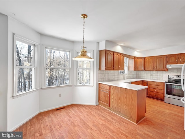 kitchen with kitchen peninsula, hanging light fixtures, light wood-type flooring, stainless steel range with electric cooktop, and decorative backsplash