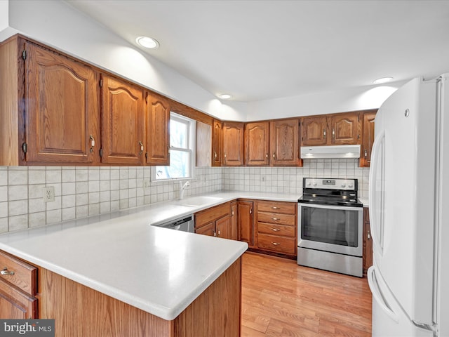 kitchen with appliances with stainless steel finishes, light hardwood / wood-style floors, sink, backsplash, and kitchen peninsula