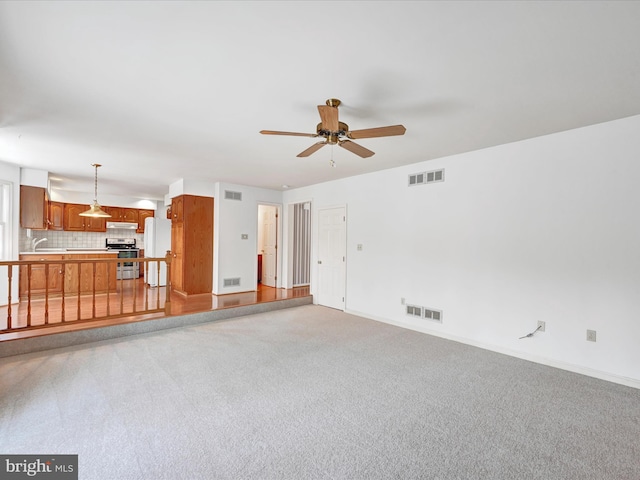 unfurnished living room featuring sink, light colored carpet, and ceiling fan