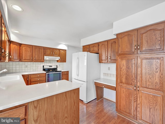 kitchen with kitchen peninsula, sink, tasteful backsplash, stainless steel range with electric stovetop, and white fridge