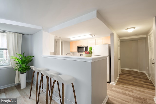 kitchen with white fridge, white cabinetry, light wood-type flooring, a kitchen bar, and kitchen peninsula