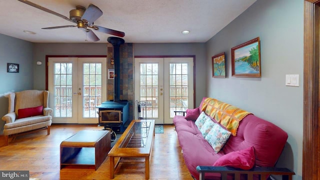 living room featuring french doors, light wood-type flooring, a textured ceiling, a wood stove, and ceiling fan