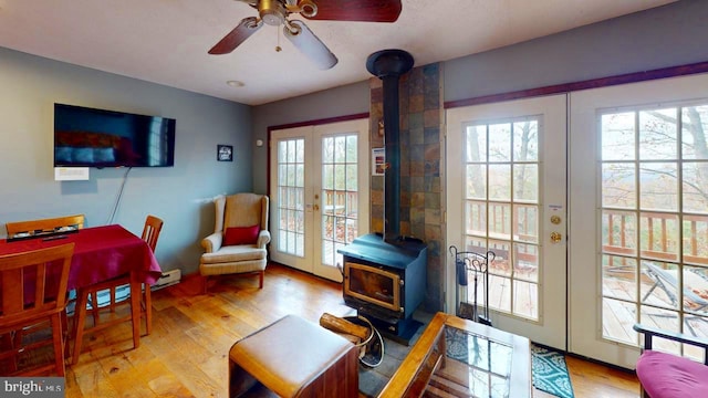 sitting room with ceiling fan, a wood stove, light hardwood / wood-style floors, and french doors