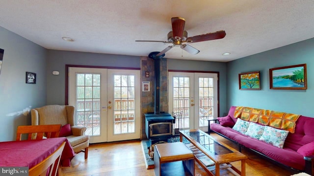 living room featuring french doors, light wood-type flooring, a wood stove, a textured ceiling, and ceiling fan