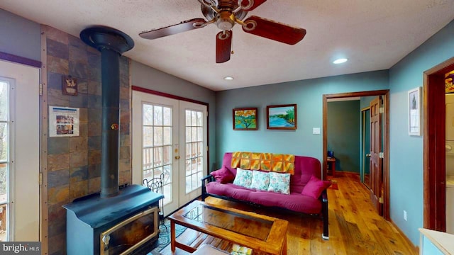 living room with french doors, wood-type flooring, a wood stove, a textured ceiling, and ceiling fan