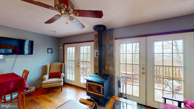 living area with french doors, light hardwood / wood-style floors, a wood stove, a textured ceiling, and ceiling fan