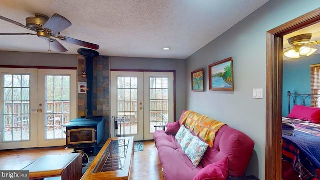 living room featuring french doors, a wood stove, a textured ceiling, ceiling fan, and light hardwood / wood-style flooring