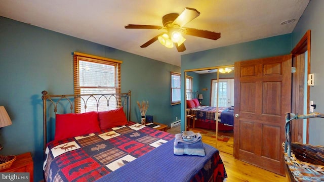 bedroom featuring a baseboard radiator, light hardwood / wood-style floors, ceiling fan, and a closet