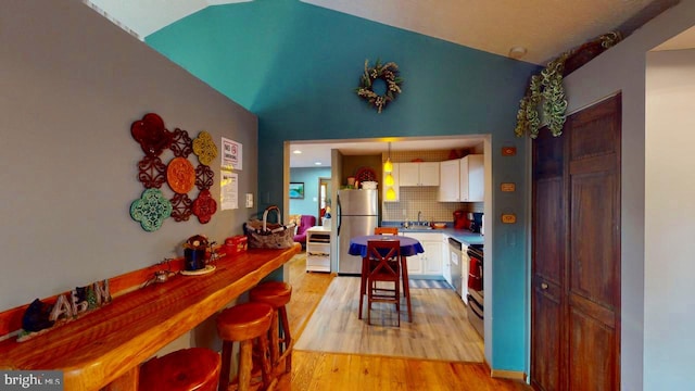 kitchen with decorative backsplash, hanging light fixtures, stainless steel refrigerator, white cabinetry, and light wood-type flooring