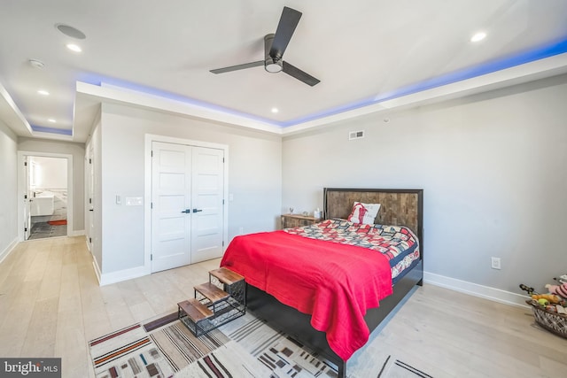 bedroom featuring a tray ceiling, ceiling fan, a closet, and light wood-type flooring