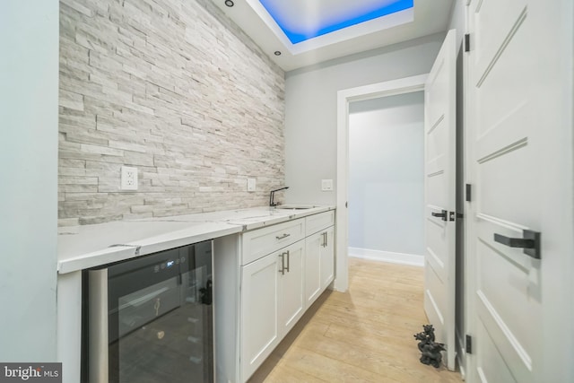 kitchen featuring light stone countertops, sink, white cabinets, light hardwood / wood-style floors, and wine cooler