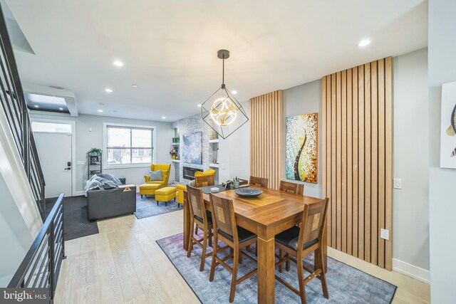 dining area with an inviting chandelier, a fireplace, and light hardwood / wood-style flooring