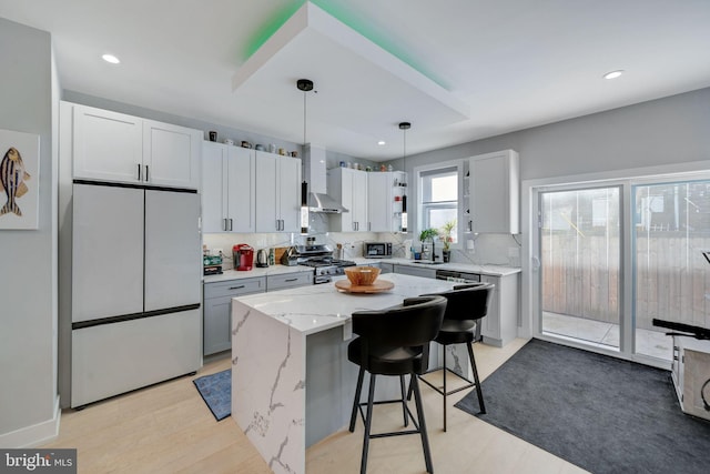 kitchen with wall chimney exhaust hood, stainless steel appliances, white cabinetry, a kitchen island, and hanging light fixtures