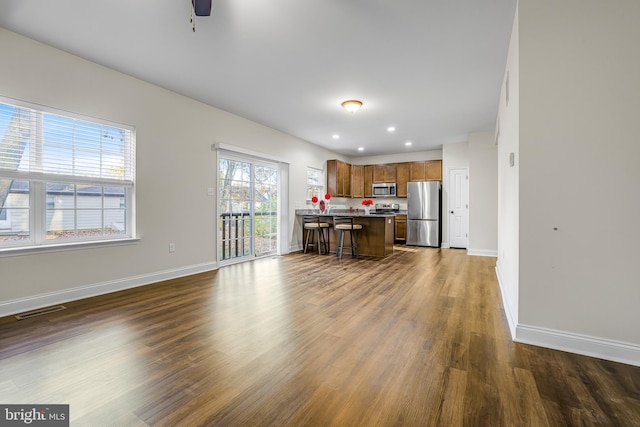 kitchen with a kitchen bar, a center island, dark hardwood / wood-style floors, ceiling fan, and appliances with stainless steel finishes