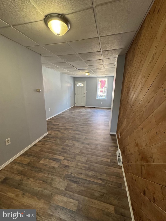 unfurnished room featuring a drop ceiling, dark hardwood / wood-style flooring, and wooden walls