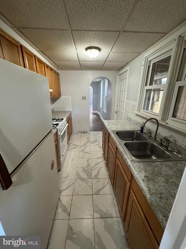 kitchen featuring a paneled ceiling, sink, white gas range oven, tasteful backsplash, and stainless steel fridge