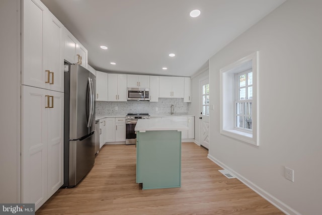 kitchen with white cabinets, a kitchen island, stainless steel appliances, and light hardwood / wood-style floors