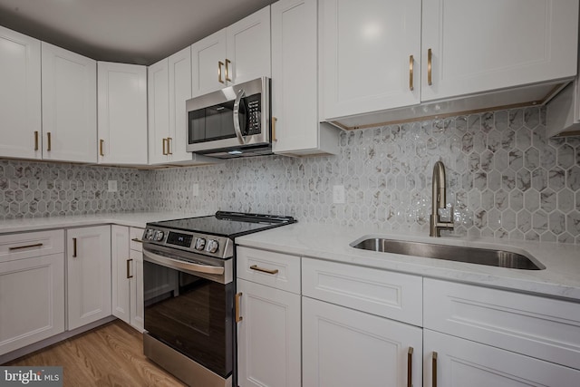 kitchen featuring white cabinets, sink, light stone countertops, appliances with stainless steel finishes, and light hardwood / wood-style floors