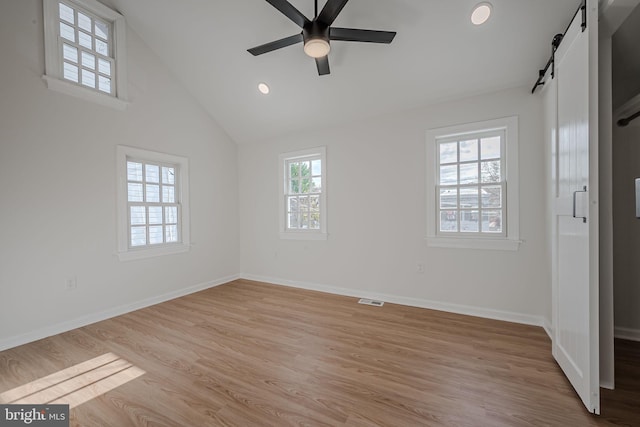 unfurnished bedroom with ceiling fan, a barn door, light wood-type flooring, and lofted ceiling