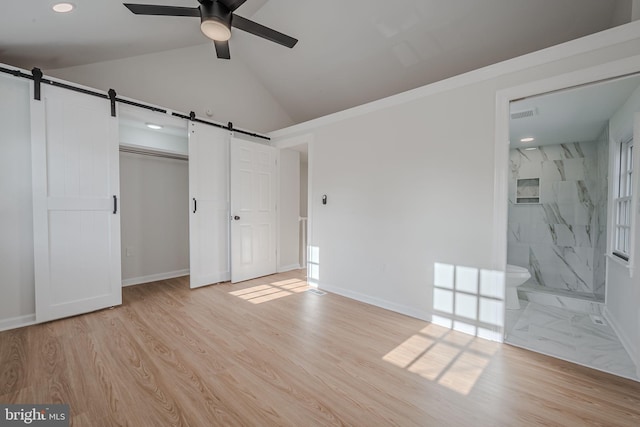 unfurnished bedroom featuring a barn door, light hardwood / wood-style flooring, ensuite bath, and ceiling fan