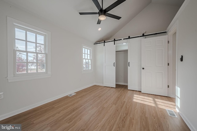 unfurnished bedroom featuring ceiling fan, a barn door, light hardwood / wood-style floors, lofted ceiling, and a closet