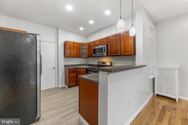 kitchen with kitchen peninsula, light hardwood / wood-style flooring, hanging light fixtures, and appliances with stainless steel finishes