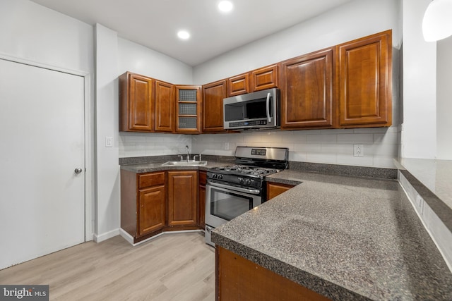 kitchen featuring backsplash, sink, appliances with stainless steel finishes, and light hardwood / wood-style flooring