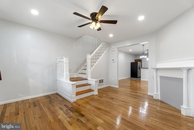 staircase featuring wood-type flooring and ceiling fan with notable chandelier