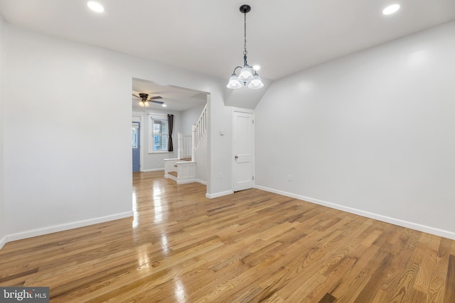 unfurnished dining area with ceiling fan with notable chandelier and light wood-type flooring