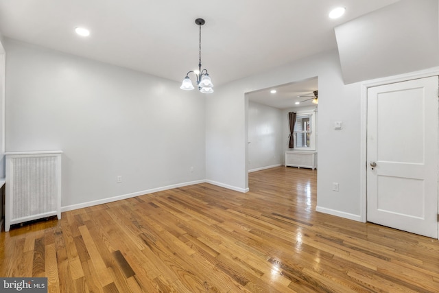 unfurnished dining area featuring radiator heating unit, wood-type flooring, and ceiling fan with notable chandelier