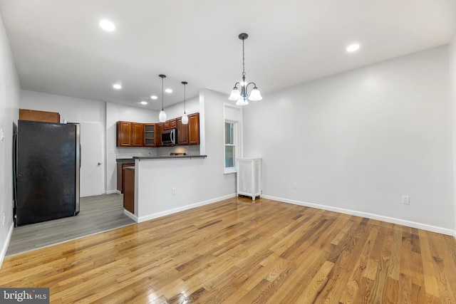 kitchen with black fridge, a notable chandelier, kitchen peninsula, pendant lighting, and light wood-type flooring