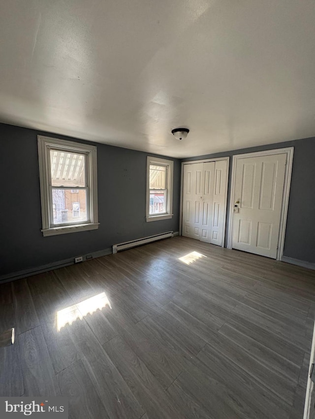 unfurnished bedroom featuring multiple windows, two closets, dark hardwood / wood-style floors, and a baseboard heating unit