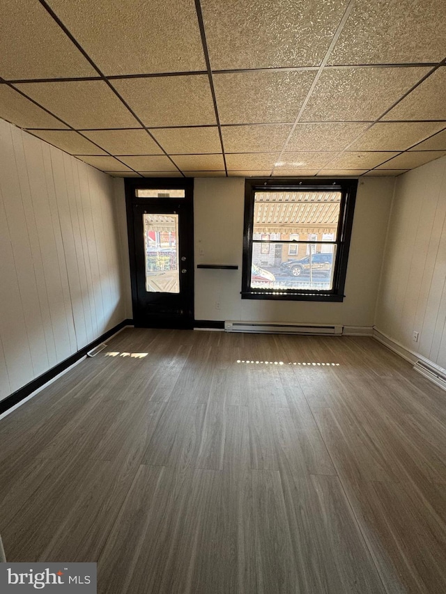 empty room featuring dark hardwood / wood-style floors, a paneled ceiling, and a baseboard heating unit