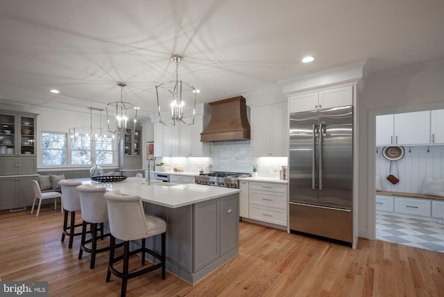 kitchen with built in fridge, hanging light fixtures, an island with sink, custom range hood, and a breakfast bar area