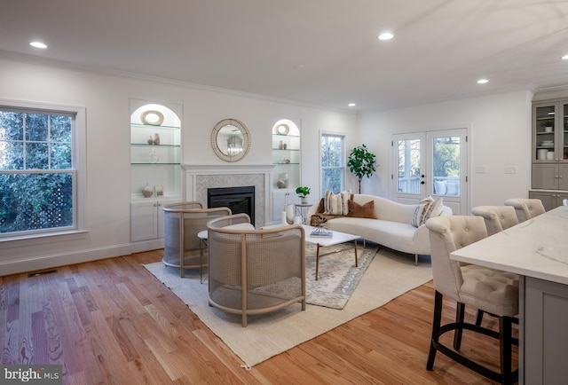 living room featuring french doors, light wood-type flooring, built in shelves, and crown molding